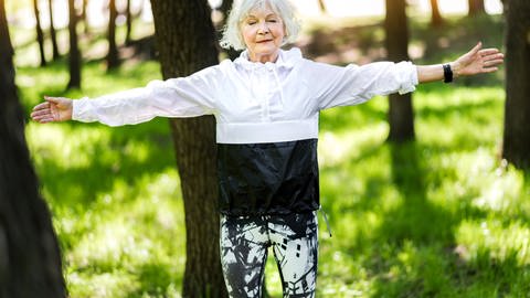 Rückwärtslaufen könnte die Balance von Parkinson Patienten verbessern | Eine ältere Frau steht mit geschlossenen Augen im Wald (Foto: IMAGO, IMAGO / Depositphotos)