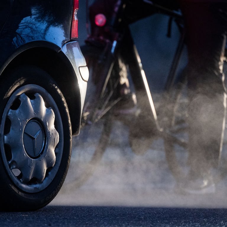 Ein Radfahrer steht neben einem Auto von Mercedes mit Dieselantrieb, dessen Abgase in der kalten Morgenluft sichtbar werden. (Foto: dpa Bildfunk, picture alliance/dpa | Marijan Murat)