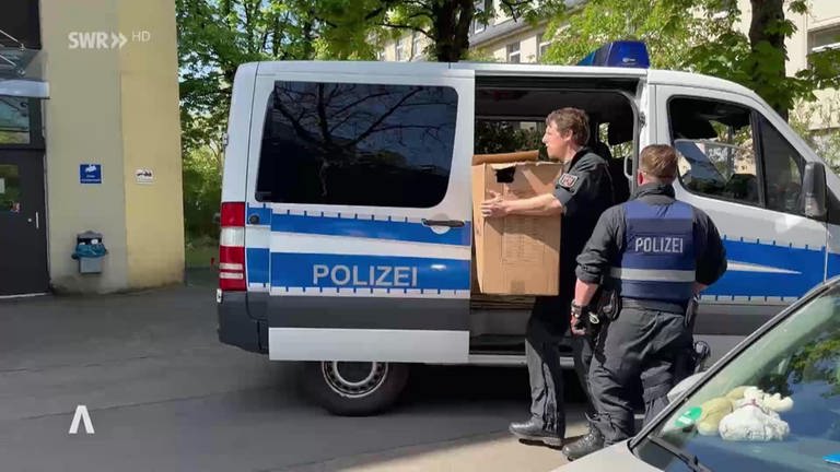 Polizisten tragen Kartons mit Beweismaterial aus dem Auto in ein Gebäude