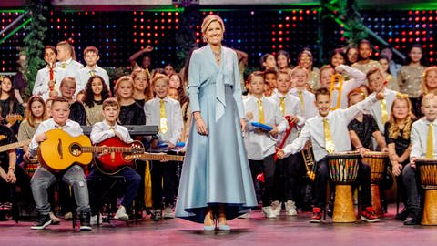 Die niederländische Königin Máxima steht in einem bodenlangen blauen Kleid umringt von jugendlichen Musikern auf der Bühne bei der TV-Aufzeichnung zur Sendung "Christmas Music Gala 2023".