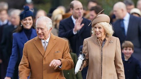 Kölnig Charles und Königin Camilla gehen zum Weihnachtsgottesdienst in Sandringham. Dahinter ist Prinz William und Prinzessin Kate mit ihren Kindern.