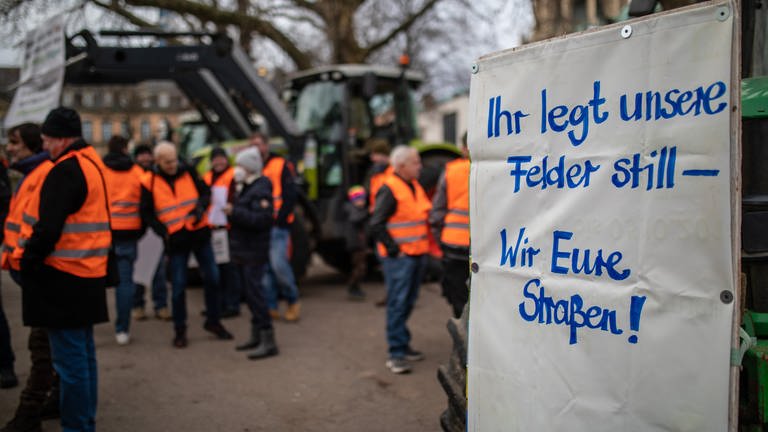 Bei einer Mahnwache vom Landesbauernverband Baden-Württemberg in Stuttgart, hängt ein Schild mit der Aufschrift "Ihr legt unsere Felder still - Wir eure Straßen" an einem Traktor.