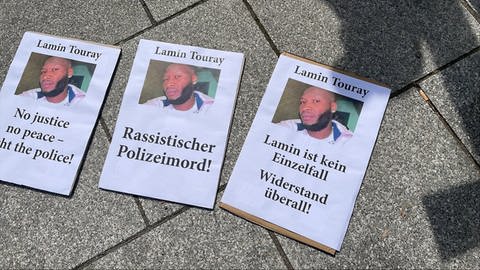 Mit Plakaten demonstrieren Menschen in Stuttgart gegen Polizeigewalt. Auslöser war der Tod des Gambiers Lamin Touray. Er starb am Ostersamstag durch mehrere Schüsse bei einem Polizeieinsatz im niedersächsischen Nienburg. 