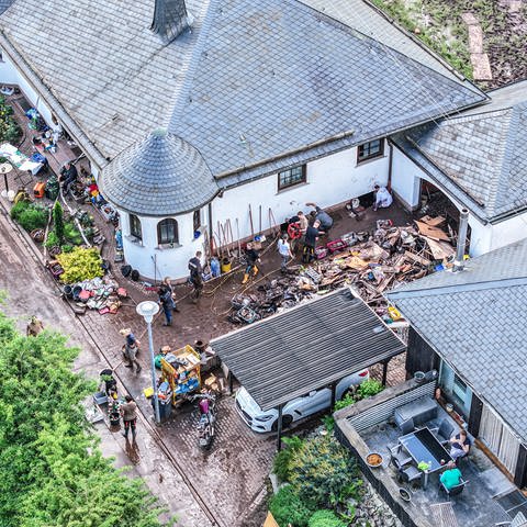 Das Luftbild zeigt Aufräumarbeiten in Kirn-Sulzbach am Tag nach dem Regen. Menschen kämpfen gemeinsam gegen Schlamm und Wasser an.