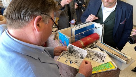 Der Mainzer Bürgermeister Günter Beck (Grüne) betrachtet alte Fotos aus der Zeitkapsel: Es sind Fotos vom Bau der Mainzer Rheingoldhalle.