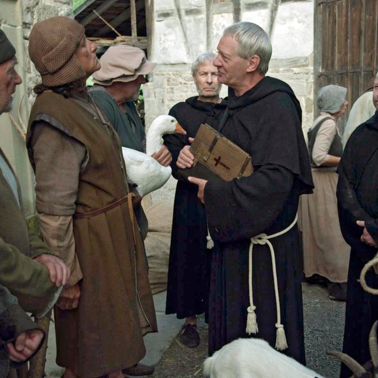 Auf einem Marktplatz steht eine Gruppe von Bauern drei Kleriker gegenüber. Die Kleriker tragen dunkle Kutten, einer von ihnen trägt eine Bibel.  (Foto: SWR, Jens Boeck)