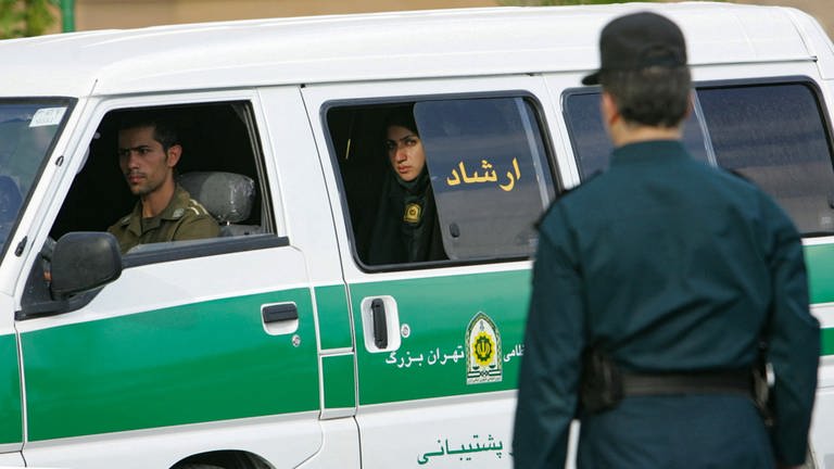 Ein Polizist und eine Polizistin sitzen in einem Minibus der iranischen Polizei. (Foto: AFP)