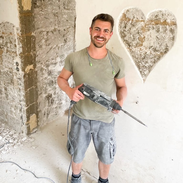 Ein junger Mann steht in Arbeitskleidung in einem von der Flut geschädigten Haus. Er hat ein Herz in die Wand gehämmert.  (Foto: SWR)