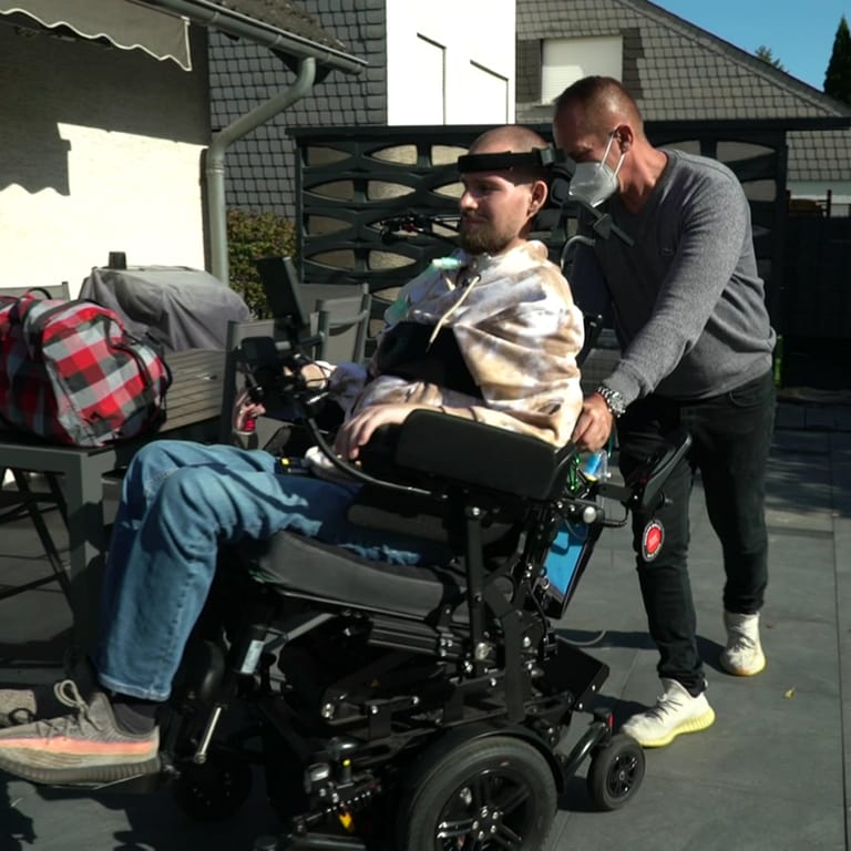 Älterer Mann schiebt jungen Mann im Rollstuhl