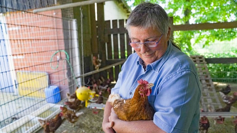 Frau mit blauer Jeansbluse und kurzen grauen Haaren hat ein Huhn im Arm. (Foto: SWR)