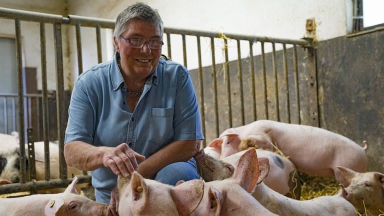 Ältere Frau mit Jeansbluse sitzt im Schweinestall und streichelt die Ferkel. (Foto: SWR)