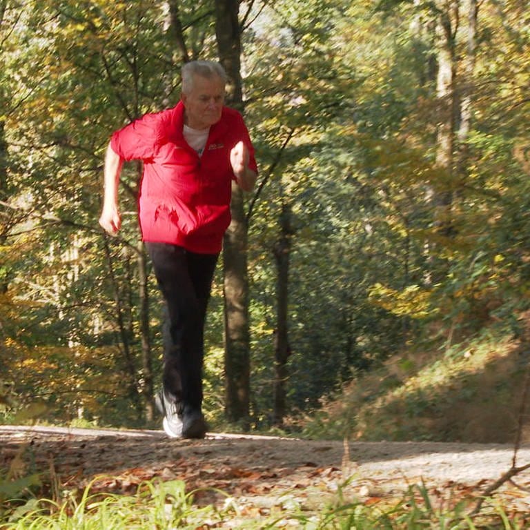 Senior in roter Jacke rennt durch den Wald