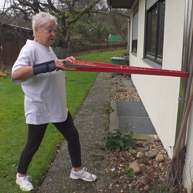 Aerobic-Trainerin Christa ist in ihrem Garten und macht Sportübungen mit einem Kraftband.  (Foto: SWR)