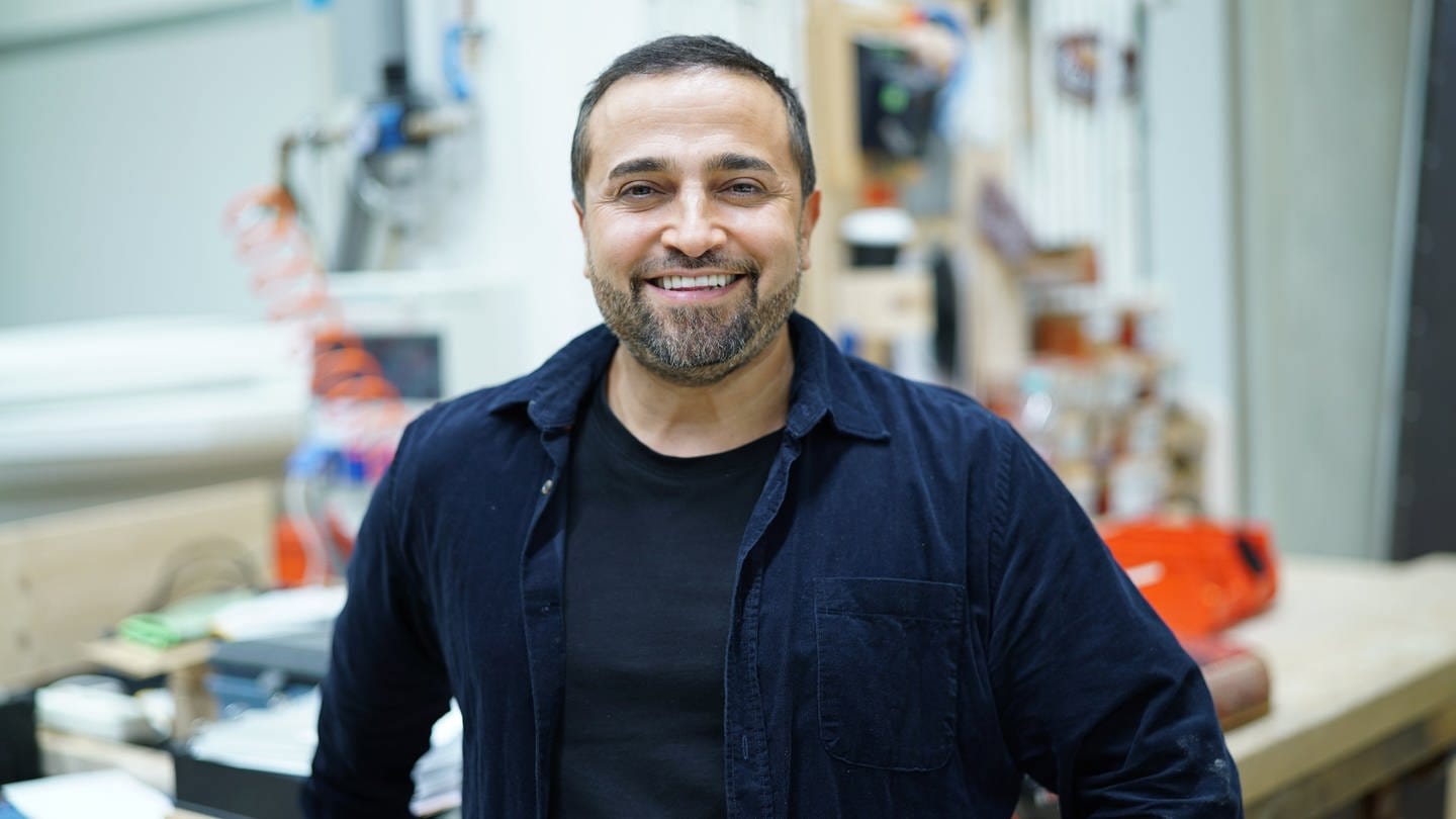 Ehemann Murat Özcan von Sallys Welt steht in einer Werkstatt und schaut lächelnd in die Kamera. (Foto: SWR)