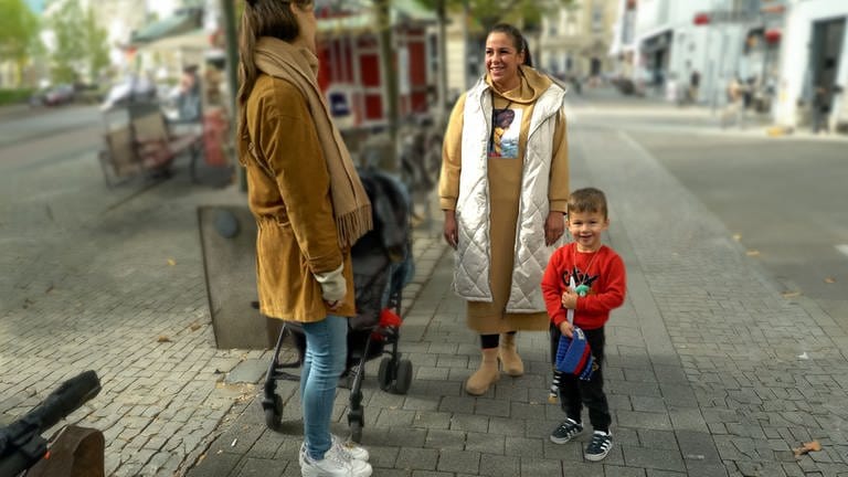 Valentina steht mit ihrem Sohn Joschua in der Karlsruher Innenstadt und unterhält sich mit Tici, die ein Mikro in der Hand hält.   (Foto: SWR)