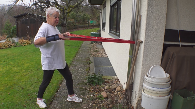 Aerobic-Trainerin Christa ist in ihrem Garten und macht Sportübungen mit einem Kraftband. 