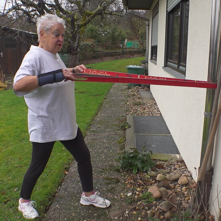 Aerobic-Trainerin Christa ist in ihrem Garten und macht Sportübungen mit einem Kraftband. 