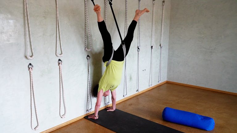 Frau macht Handstand mit Gurten an einer Wand auf einer Yogamatte.