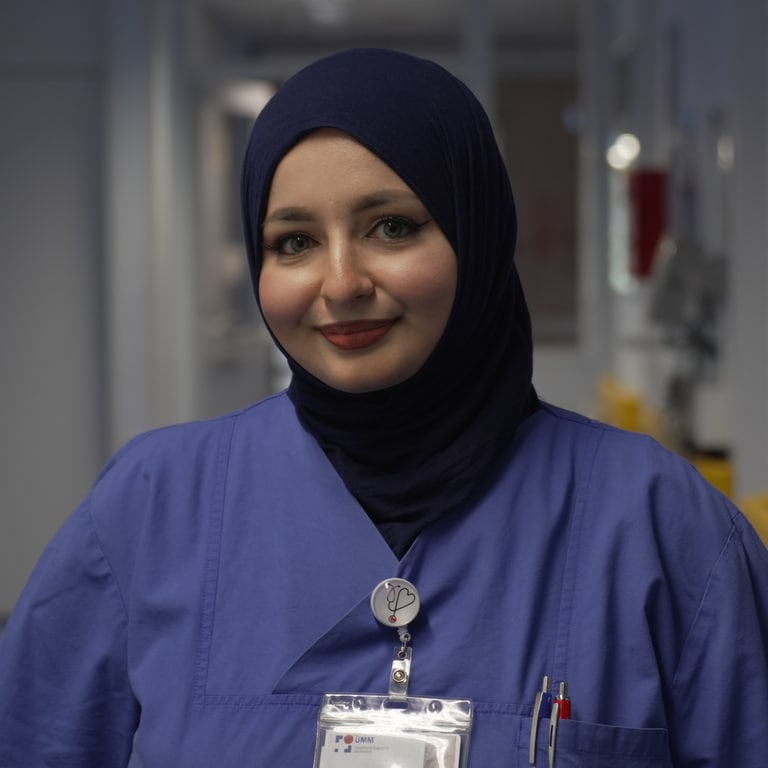 Eine Krankenpflegerin mit Kopftuch steht im Krankenhausflur und lächelt