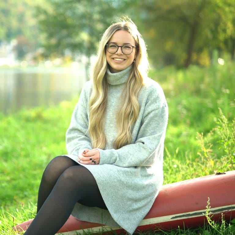Junge Frau am Flussufer auf dem Rumpf eines Ruderbootes sitzend (Foto: SWR)