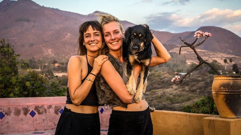 Zwei Frauen mit einem Hund auf dem Arm stehen vor Bergkulisse