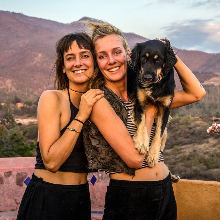 Zwei Frauen mit einem Hund auf dem Arm stehen vor Bergkulisse