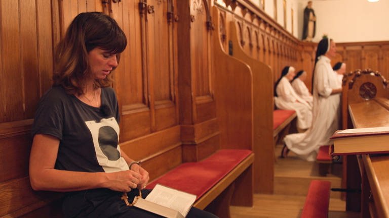 Frau in Tshirt und Jeans betet zwischen Nonnen Rosenkranz im Kloster