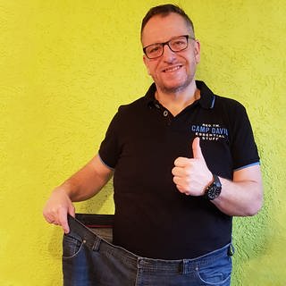 Mann hält eine Jeans vor sich, die doppelt so breit ist wie er selbst (Foto: SWR)