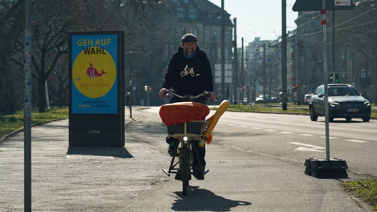 Wolfgang, schwarzer Pulli, sitzend auf seinem Lastenrad, fährt eine Straße in der Mannheimer Innenstadt entlang.  (Foto: SWR)