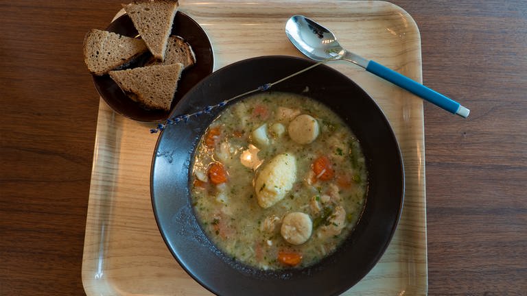 Suppe im Suppenteller von oben fotografiert mit Scheiben Brot und Löffel daneben.