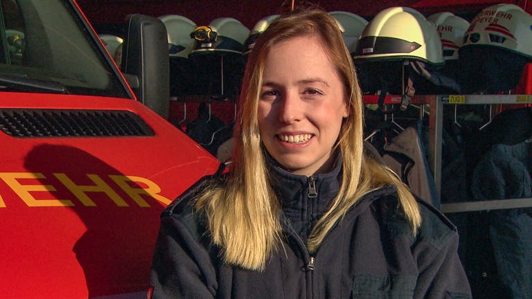 Feuerwehrfrau Selina, jung, 22 Jahre, vor einem Feuerwehrauto