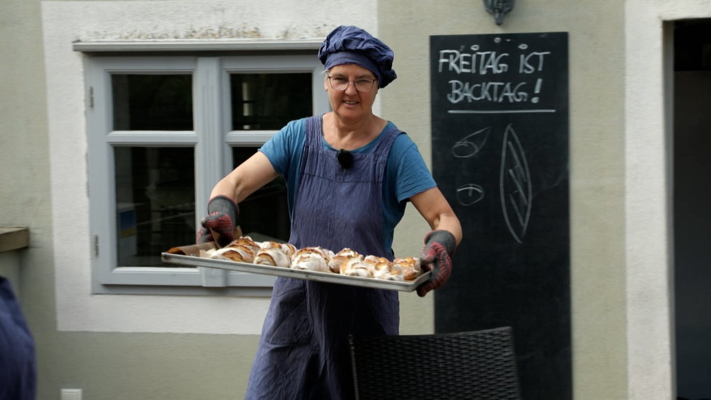 Frau mit blauer Mütze und Schürze trägt Blech mit Brot. (Foto: SWR)