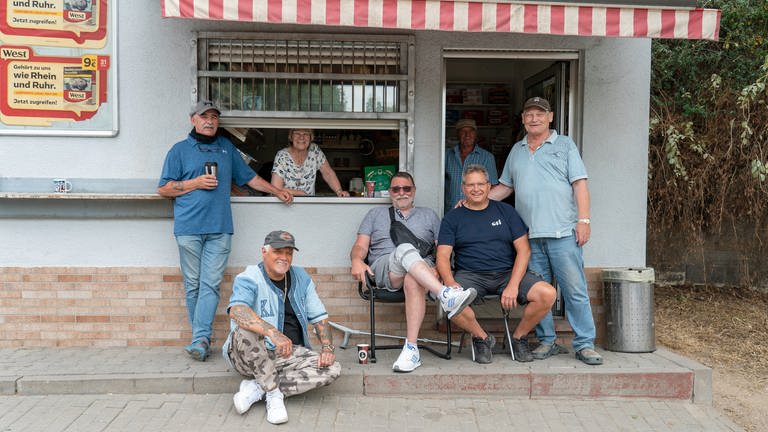 Eine Gruppe von Männern vor einem Kiosk, einige stehen, andere sitzen. (Foto: SWR)