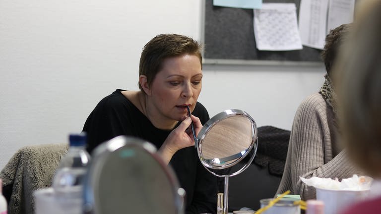 Eine Frau mit kurzen Haaren schminkt sich vor dem Spiegel die Lippen. (Foto: SWR)