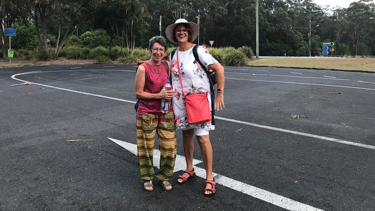Zwei ältere Damen mit Rucksäcken auf einem Parkplatz.
