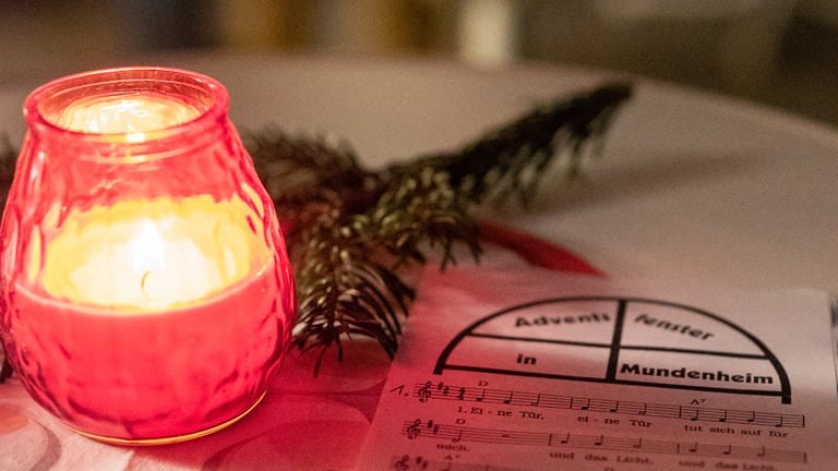 Auf einem weißen Stehtisch liegen ein Liedblatt, ein Tannenzweig und eine Kerze leuchtet. (Foto: SWR)