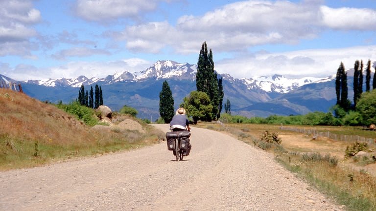 Ein Fahrradfahrer von hinten auf einer Straße vor Bergpanorama.