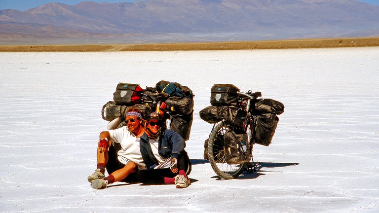 Zwei Menschen sitzen vor ihren voll bepackten Fahrrädern in der Atacama Wüste.
