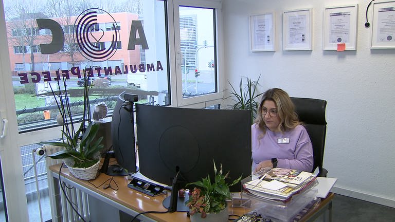 Junge Frau mit lila Pullover sitzt an einem Computer und arbeitet. 