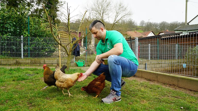 Benjamin, Mann, der drei Hühner füttert auf einer Wiese (Foto: SWR)