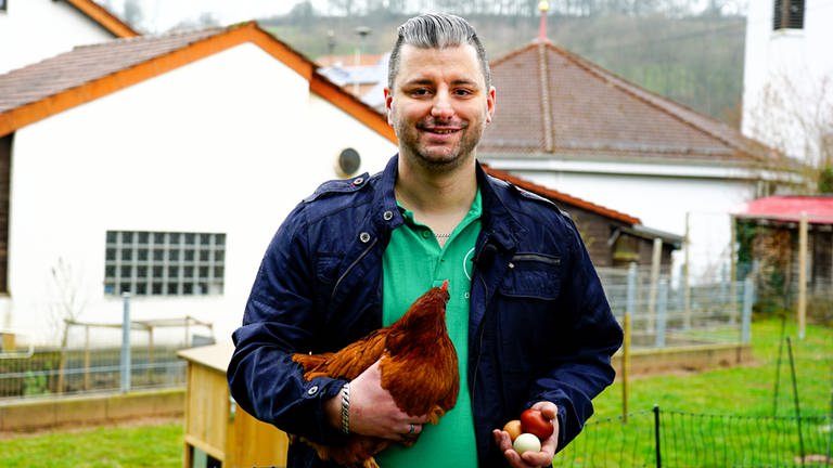 Benjamin, Mann mit braunem Huhn auf dem Arm und drei Eiern in der Hand