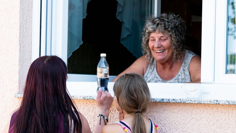 Frau steht am Fenster und redet mit einer anderen Frau und einem Kind über die Fensterbank. (Foto: SWR)