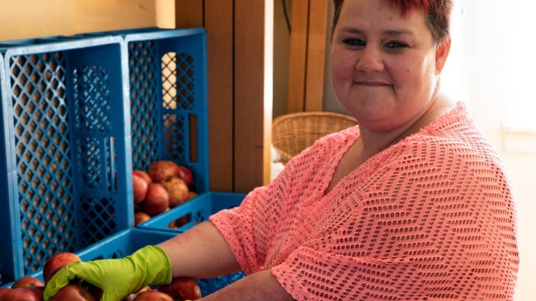 Eine Frau steht vor einigen Kisten, die mit Äpfeln gefüllt sind.