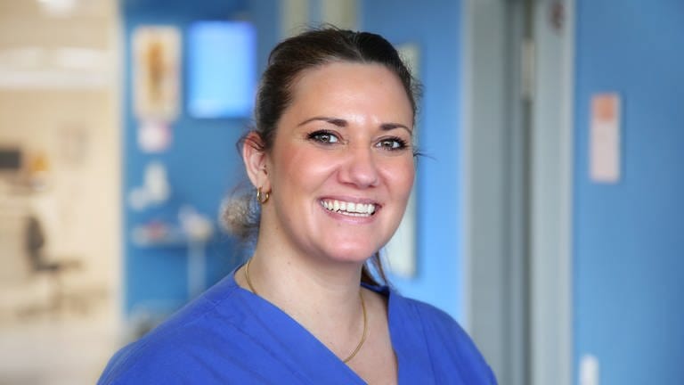 Natalia ist medizinische Fachangestellte im Bereich der zentralen Notaufnahme in Ludwigshafen. Sie steht in der Notaufnahme und lächelt in die Kamera. 