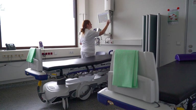 Junge Frau mit roten Haaren und weißer Arbeitskleidung in einem Krankenhausbehandlungsraum. Sie stellt einen Monitor ein. (Foto: SWR)
