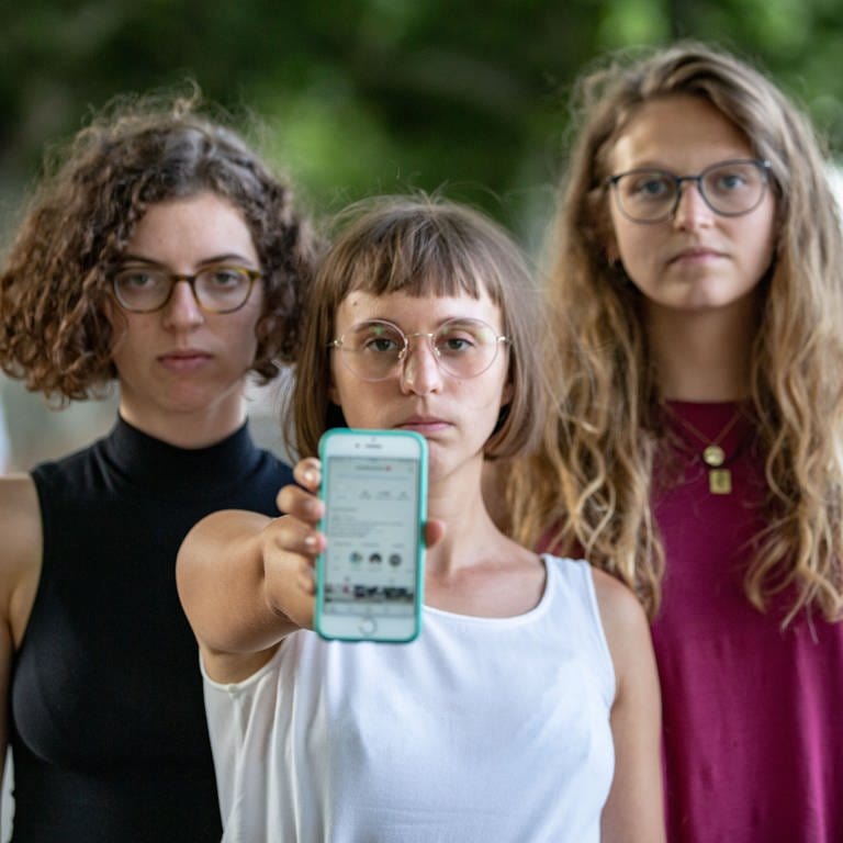 Drei Frauen mit ernster Miene halten Smartphone in die Kamera