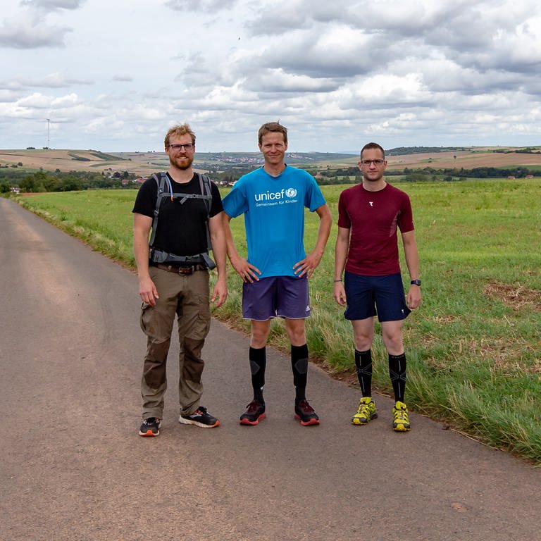 Drei junge Männer stehen in Wanderklamotte im Feld (Foto: SWR)