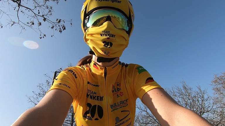 Lea fährt auf dem Rennrad. Ihr Gesicht ist hier der gelben Maske und verspiegelten Brille versteckt. (Foto: SWR)