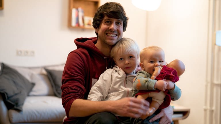 Junger Mann mit zwei kleinen Kindern auf dem Arm