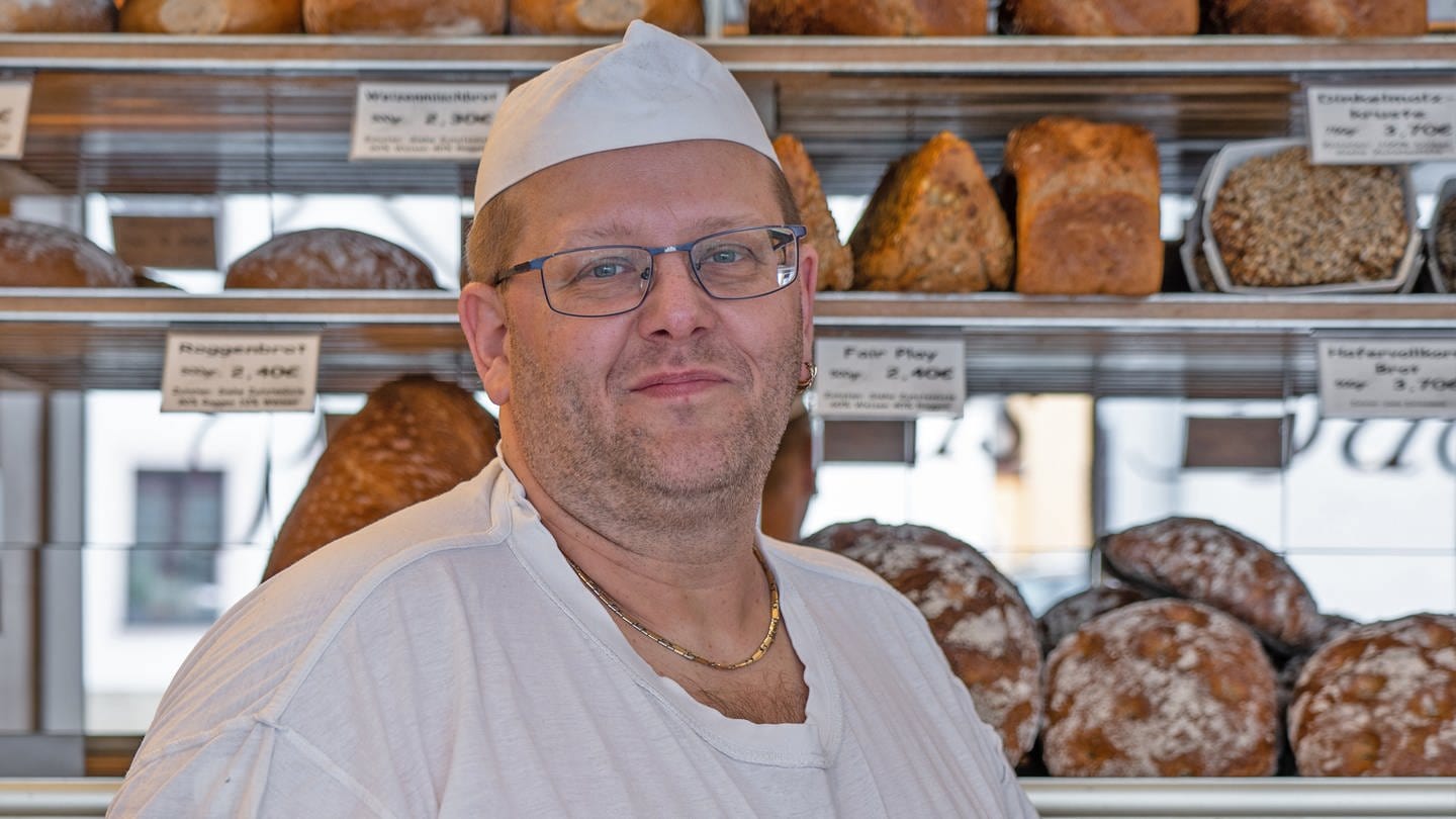 Bäcker mit weißer Mütze vor der Auslage seiner Bäckerei.